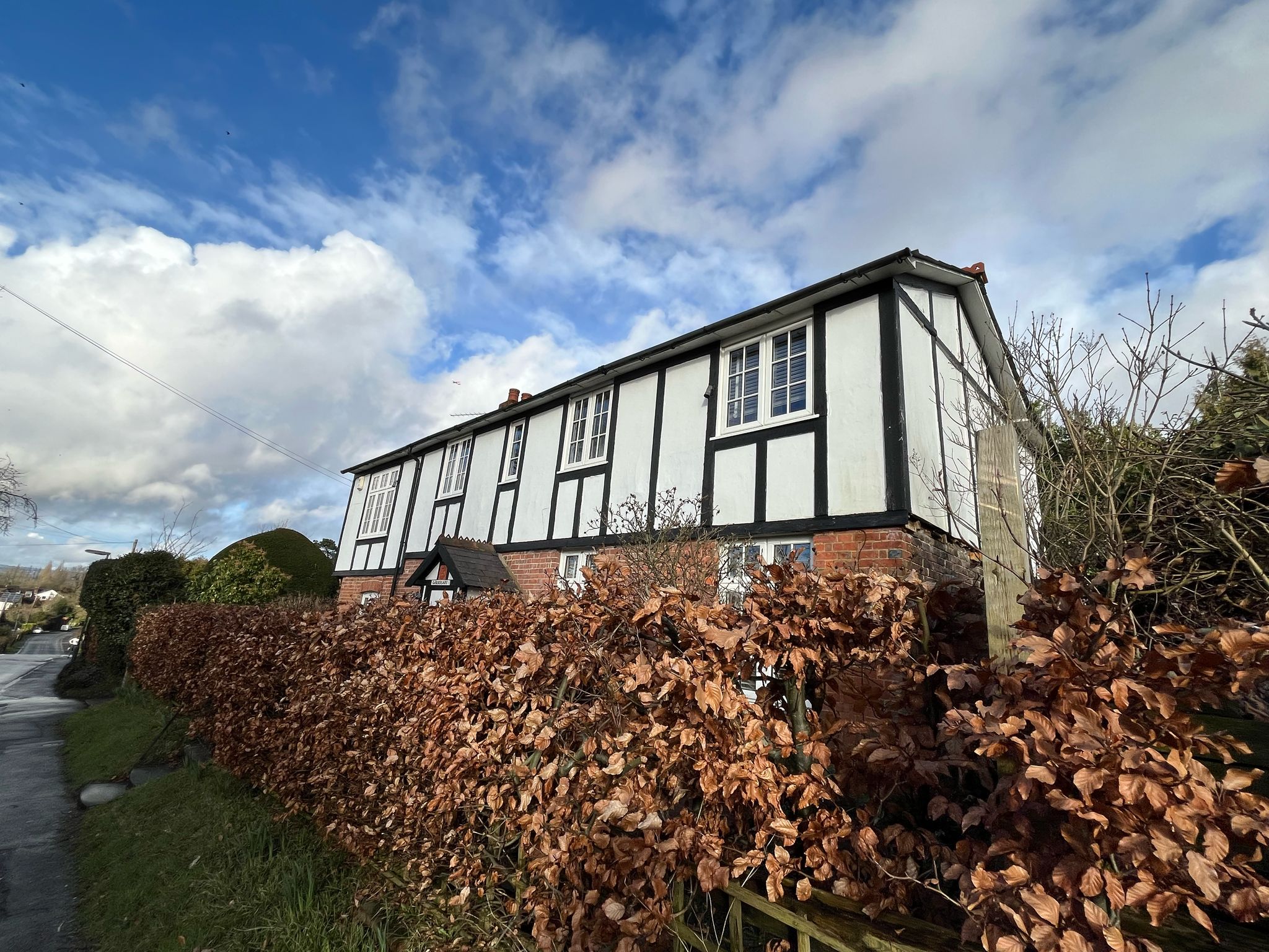 Building behind mature hedge fronting onto a road with a view along a winding road.